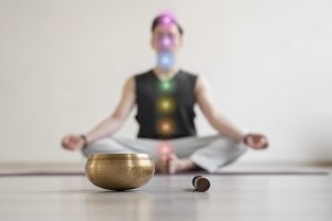Young man practicing meditation indoors, 7 chakra's superimposed over the person.