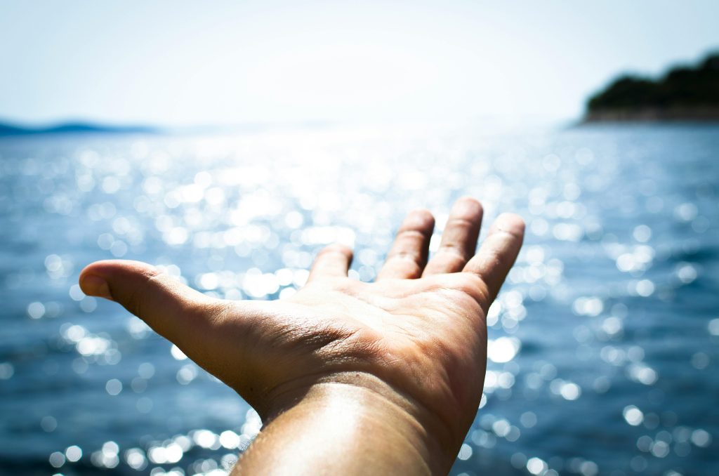 Open, extended hand on ocean background
