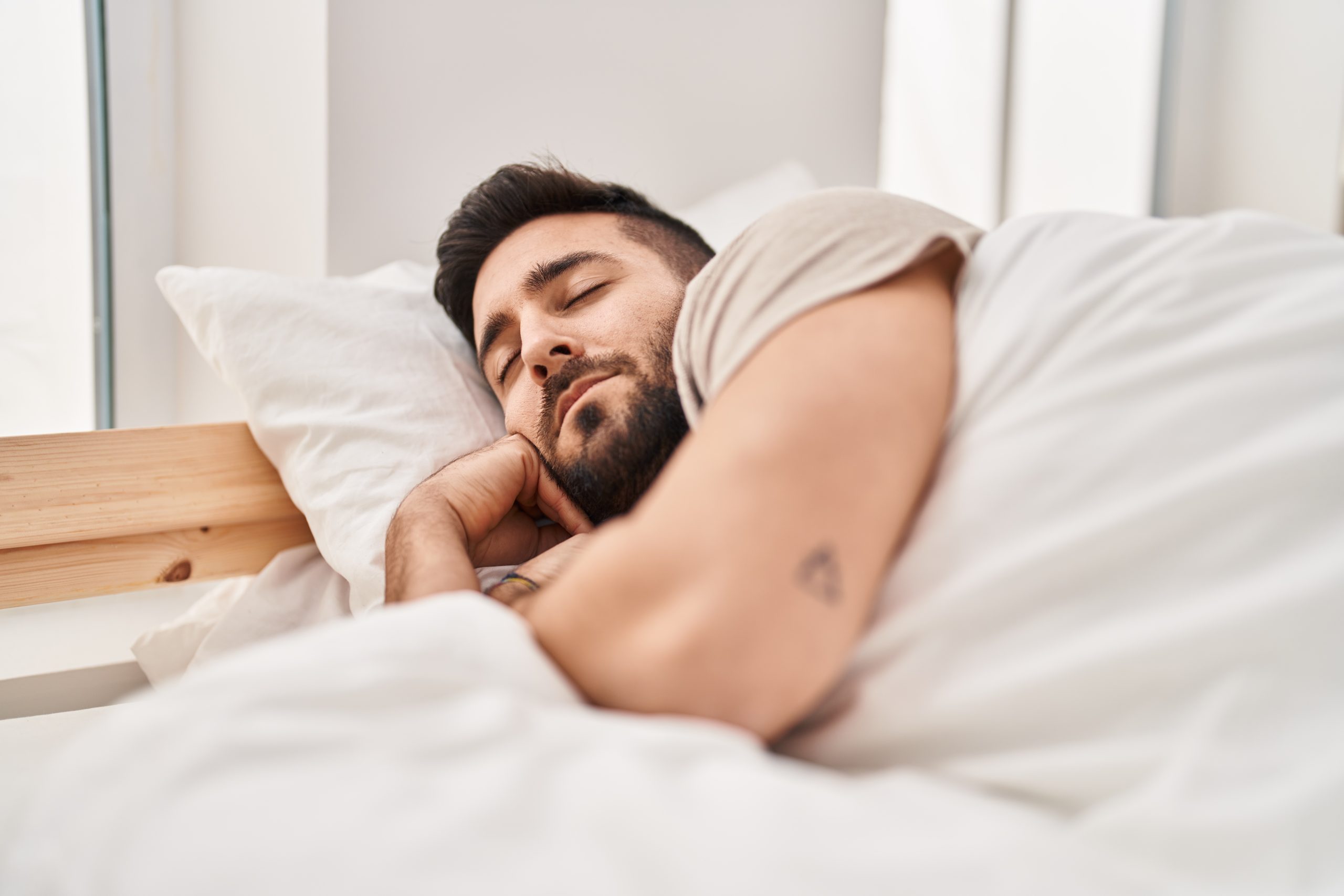 Man laying in bed during day, appears to be resting or sleeping
